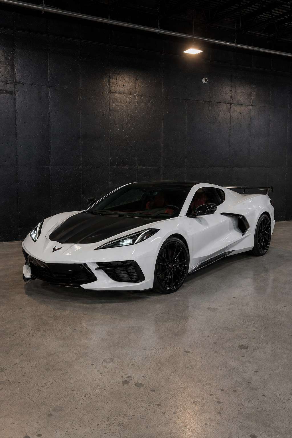 White Chevrolet Corvette C8 with an exposed carbon fiber hood, front three quarter in a dark studio