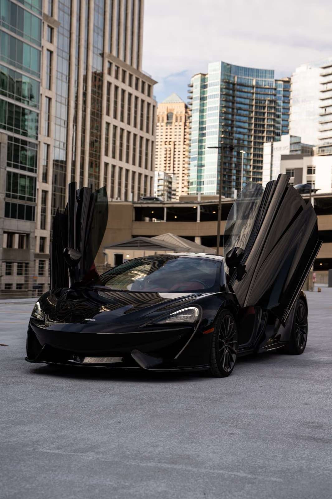 Black McLaren 570GT with the doors up on an Atlanta parking deck, Buckhead towers behind