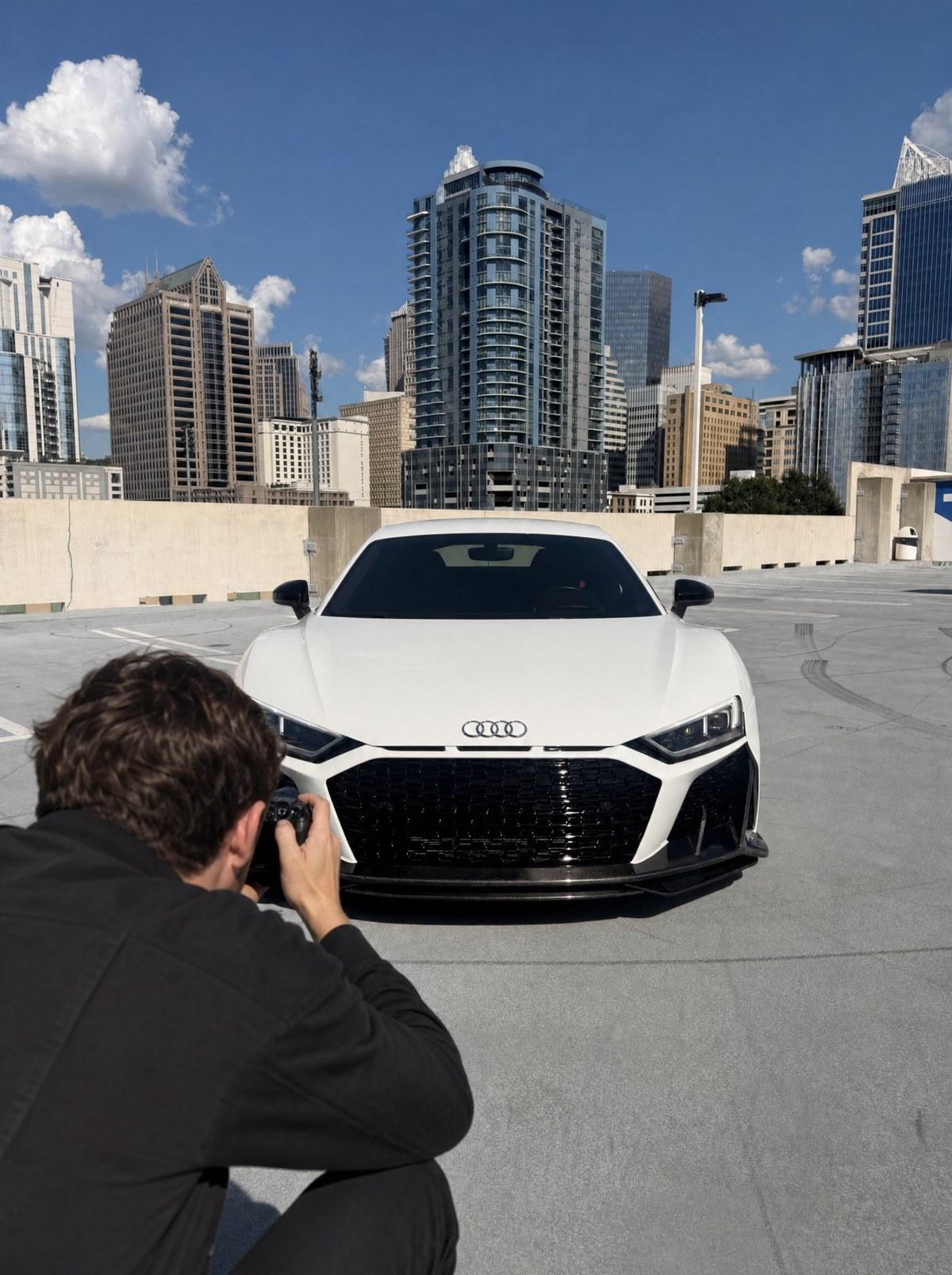Professional photographer crouched low shooting a white Audi R8 on a Midtown Atlanta rooftop deck