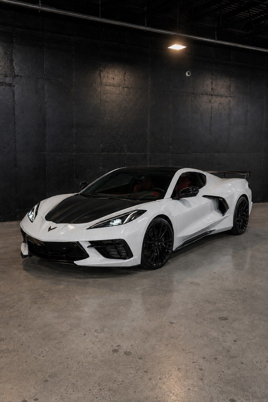 White Chevrolet Corvette C8 with an exposed carbon fiber hood, front three quarter in a dark studio