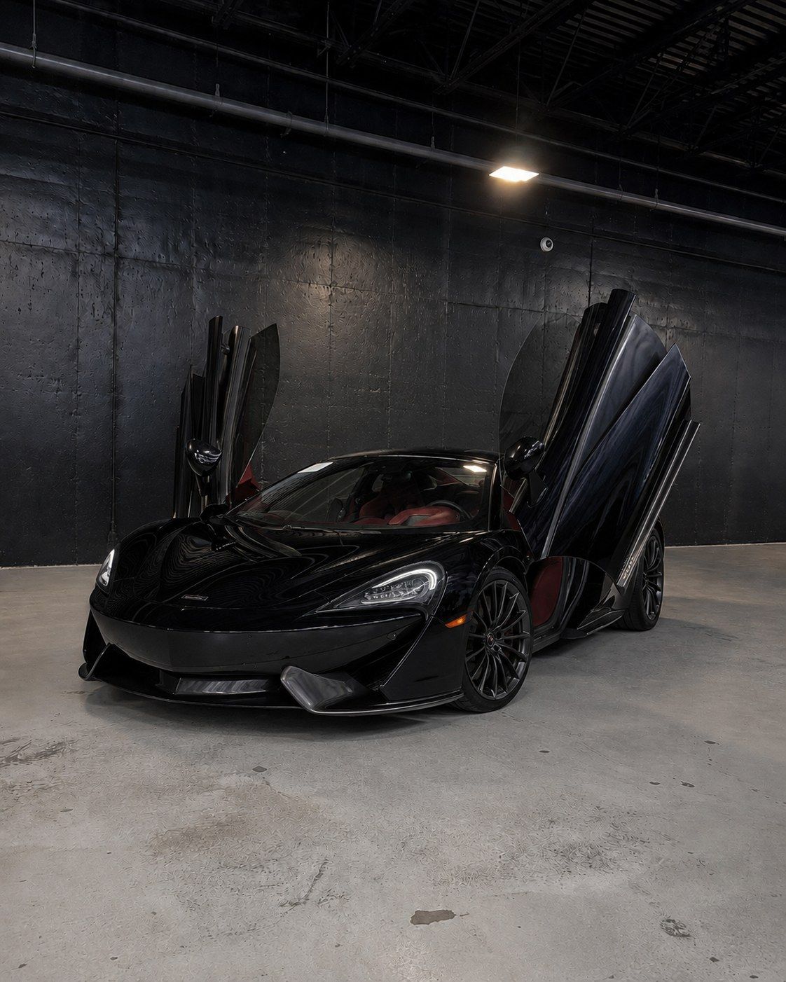 Black McLaren 570GT with both dihedral doors open showing the red interior, front three quarter in a dark studio