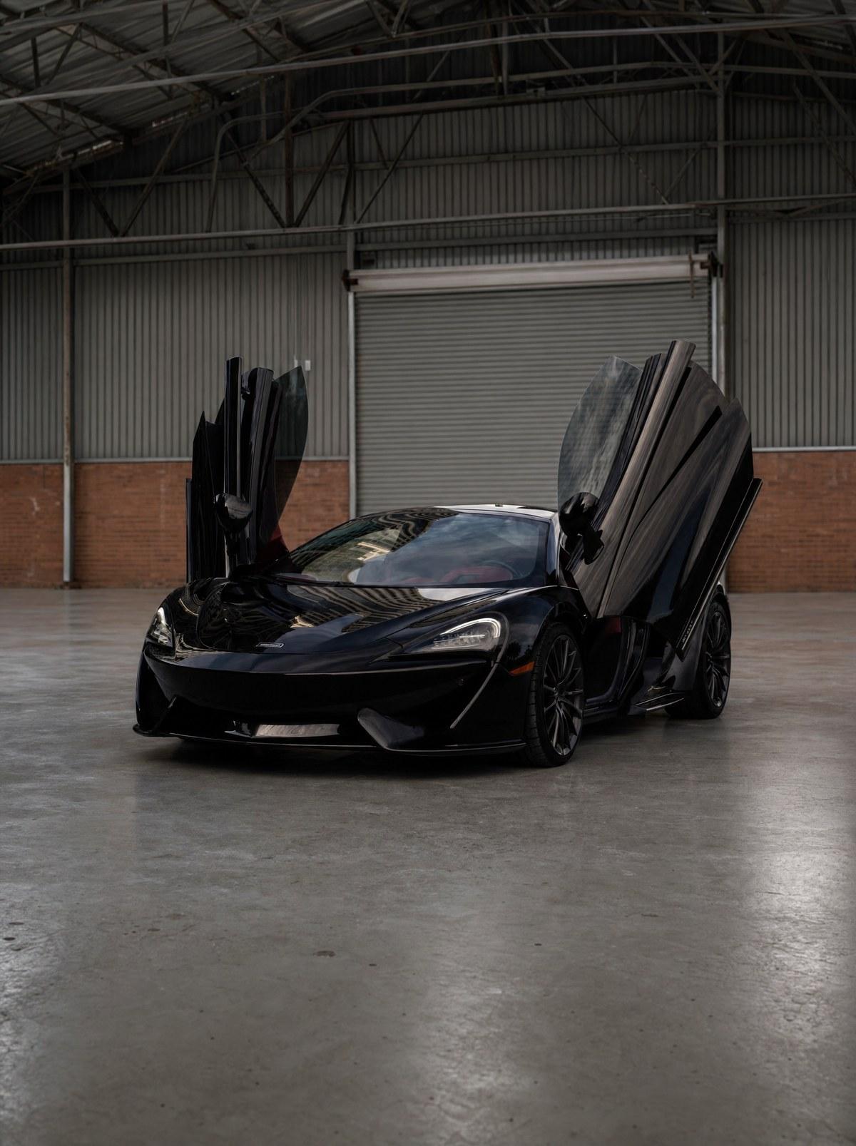 Black McLaren 570GT with both doors open in an Atlanta warehouse, set up for a music video shoot
