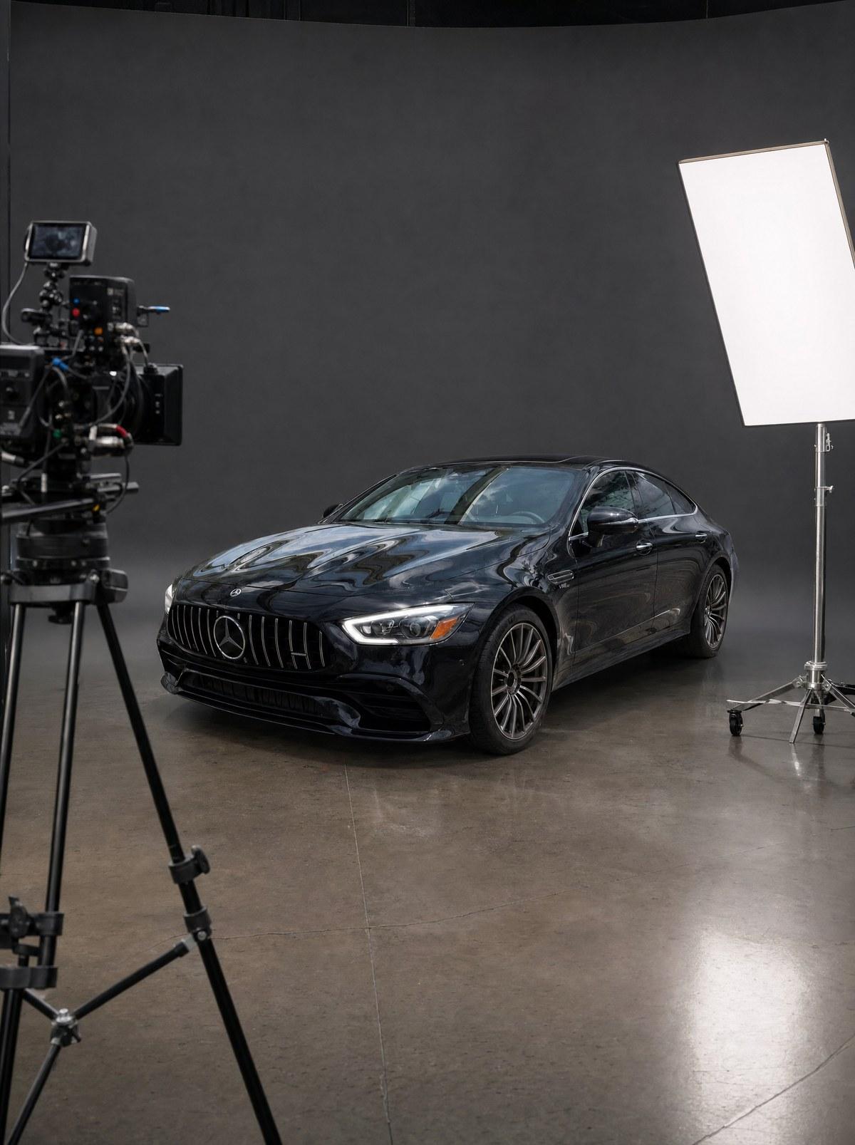 Black Mercedes-AMG GT 43 on a film soundstage with a cinema camera on a tripod and a lighting panel